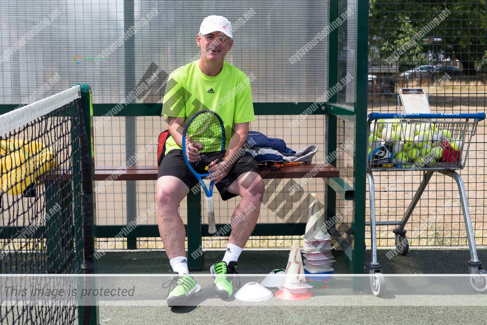 Tennis coach, Julian Cousins sitting on a bench at a tennis court holding a racket
